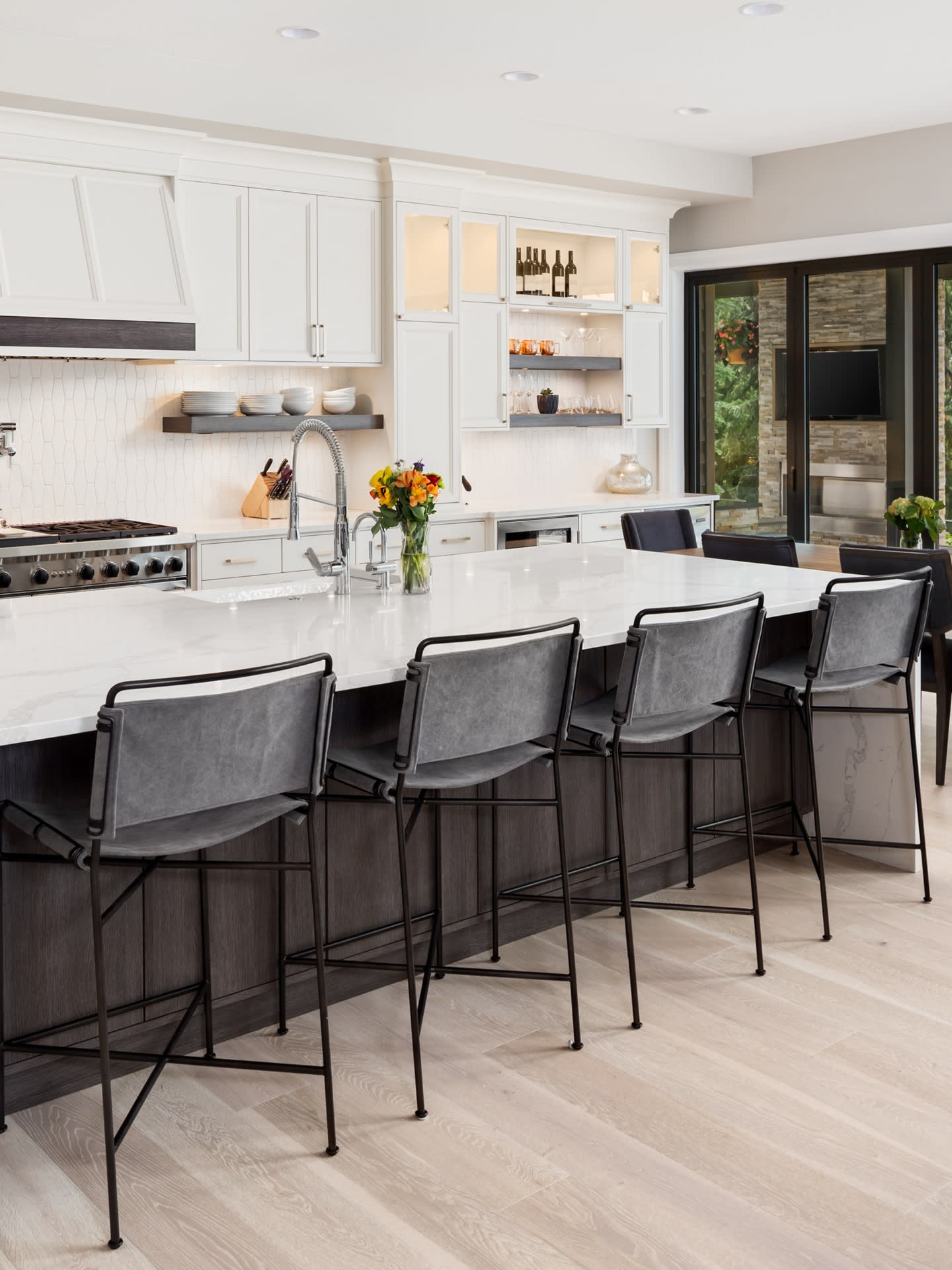 A kitchen with a large island and four bar stools next to it. The island is made of wood and has a countertop made of granite. 