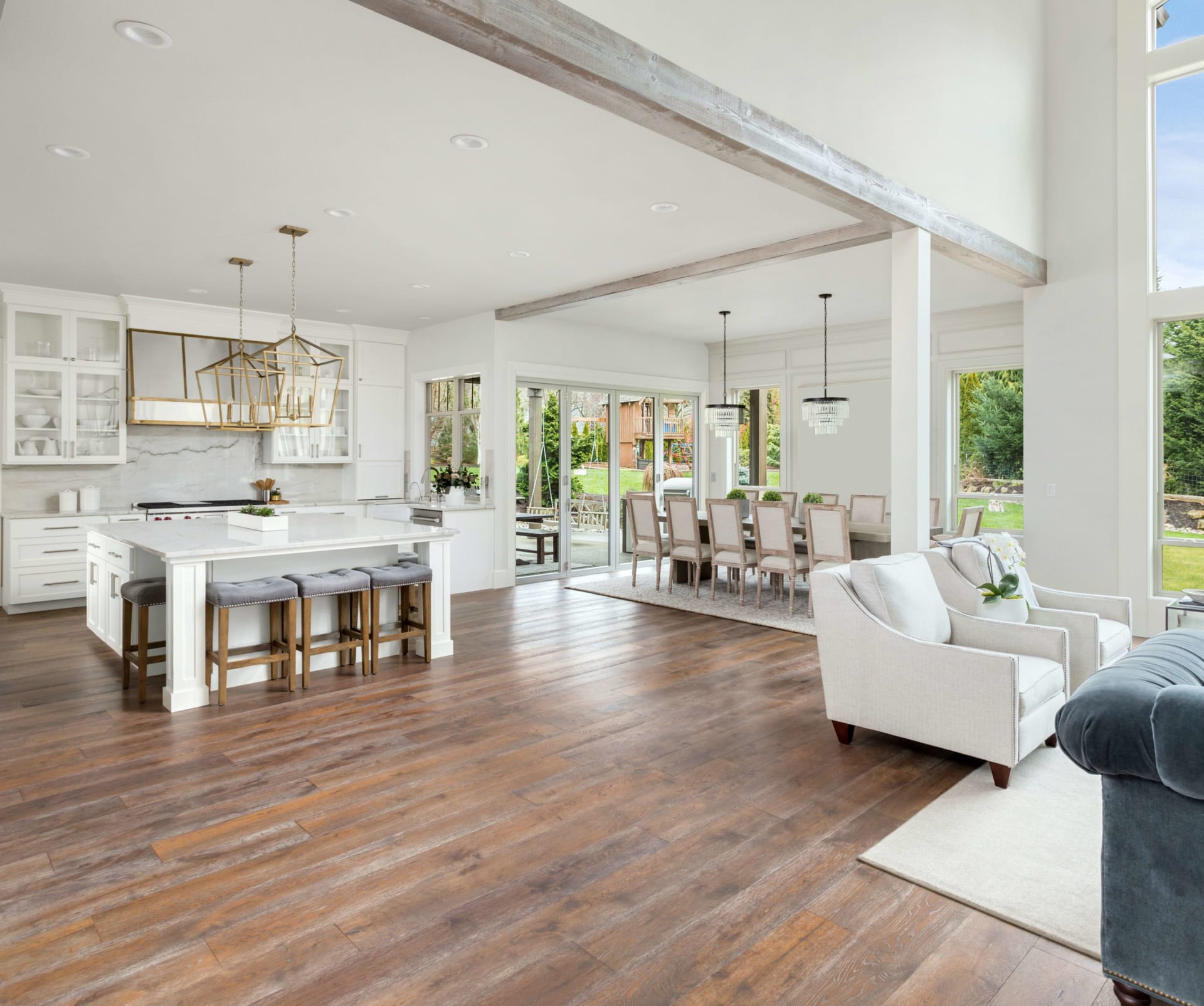 A modern farmhouse with an open floor plan, wooden floors, couches, a dining area, a kitchen, and a doorway to a patio.