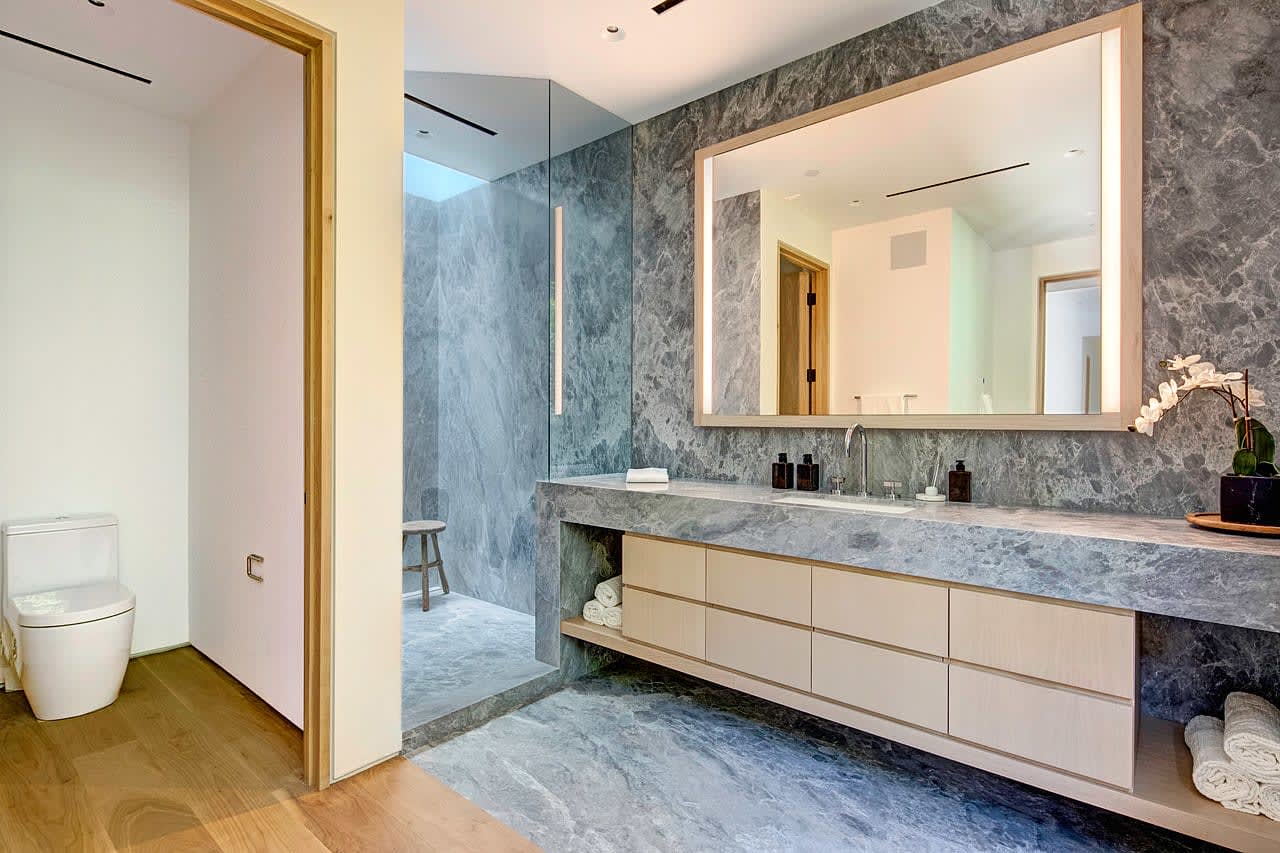 A bathroom with a marble sink, a toilet, and mirror