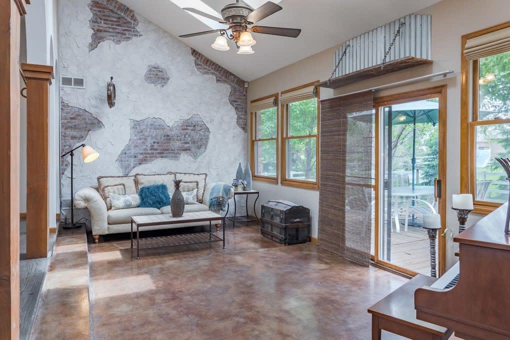 Living room with a couch, coffee table, piano, windows, and a sliding glass door overlooking a deck and trees.