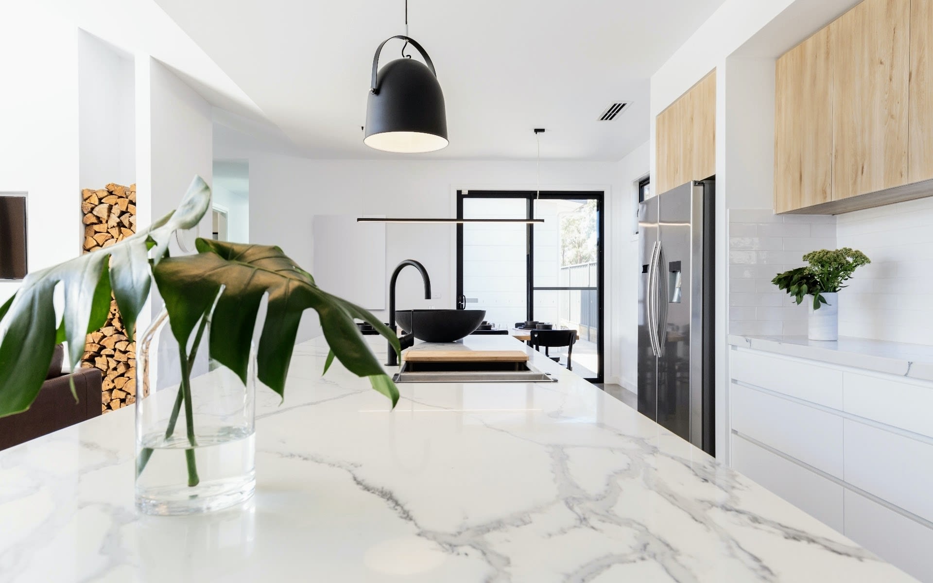 A close-up of a marble countertop in a modern kitchen. The countertop is white with subtle gray veins. There is a vase of flowers on the island.