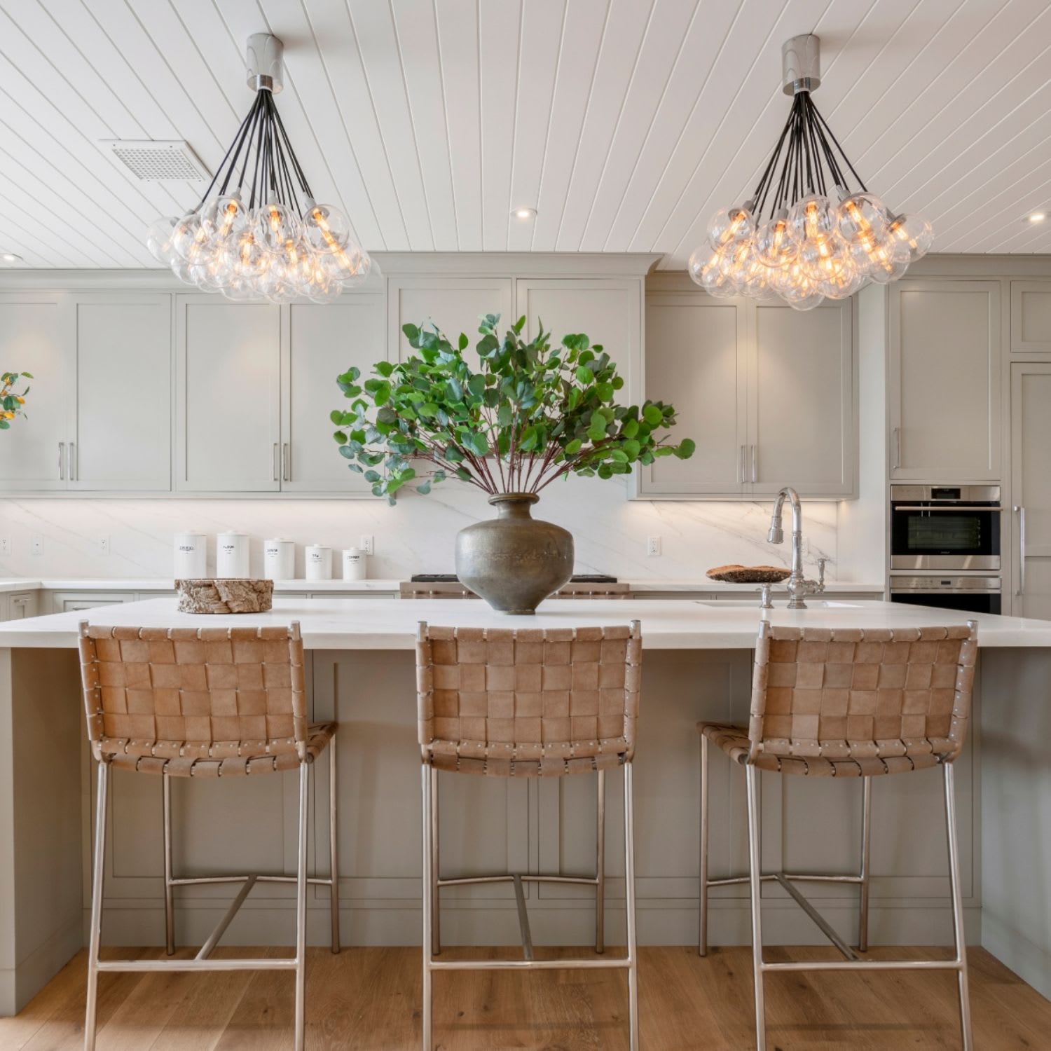 Modern kitchen with light granite bar, stainless appliances, white cabinets, and a plant-filled vase on the countertop.