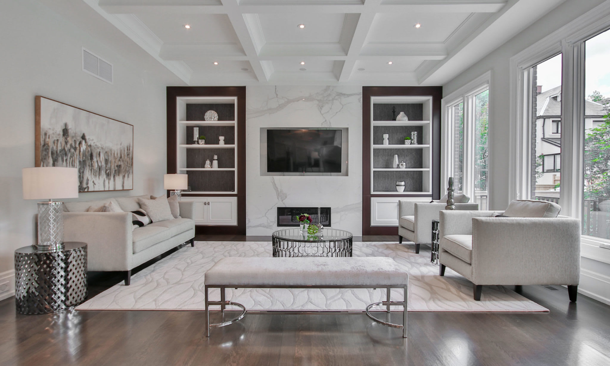 A brightly lit living room with a comfortable couch, two armchairs, a coffee table, a rug, and a TV.