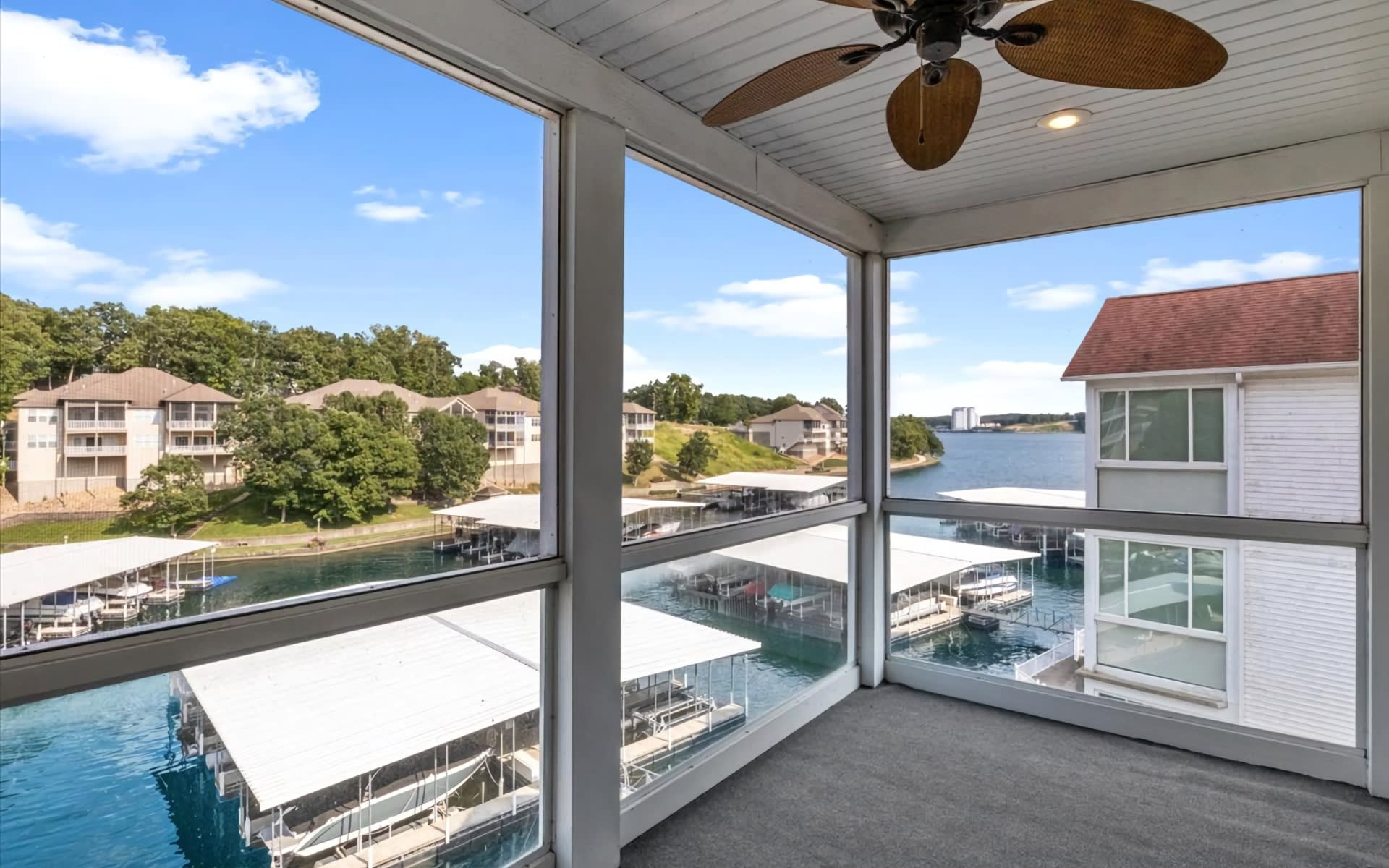 A screened-in porch with a ceiling fan overlooking a marina on Lake of the Ozarks